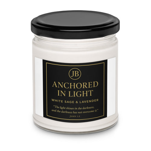 “Single ‘Anchored in Light’ candle with black lid, featuring a sleek black and gold label with scripture John 1:5. White Sage & Lavender scent in a clear glass jar, centered on a white background for a minimal, luxury presentation.”